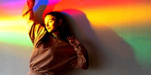 woman standing against a wall, a rainbow over her body