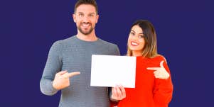 man and woman smiling and pointing at paper they're both holding onto