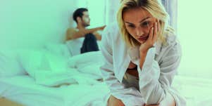 unhappy girl sitting on bed with boyfriend behind her