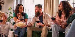 Diverse people sitting in a living room enjoying wine and popcorn together