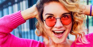 Free spirited woman in pink with funky shades smiles at camera