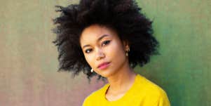 Black woman with natural hair in front of a tonal background, looking thoughtful and pleasant