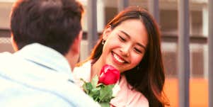 young Asian woman smiling as her boyfriend hands her a rose