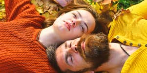 man and woman lying in autumn leaves looking up at sky together