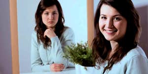 woman smiling at the camera while her mirror image gives her a mean look