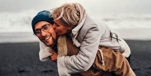 man gives woman a piggyback ride on a wintery beach