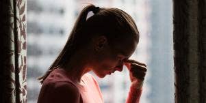 woman in ponytail pinching the bridge of her nose in front of window