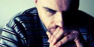 upset man looking down and thinking over folded hands