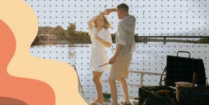 Couple dancing on pier while grilling dinner at sunset