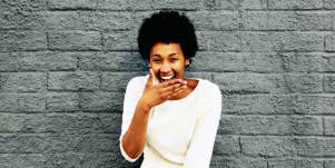 Black woman laughing in front of a brick wall