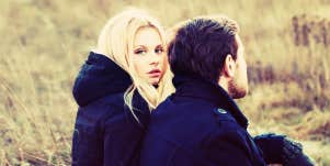 couple in a field, blonde woman looks right at camera while man looks away