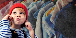 A young child is next to a rack of clothing.