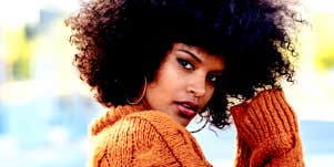 young Black woman with natural hair looks at camera in orange sweater