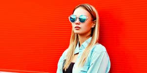 blonde woman in sunglasses looking angry against red wall