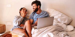 couple sitting in guy's bed with laptop and pizza