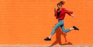 woman jumping over sidewalk crack orange background