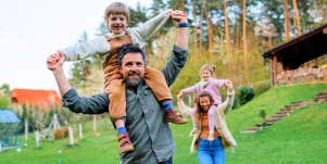 dad carrying child on shoulders with mom and sister in background