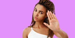 beautiful woman in front of purple background holding up her hand to say no