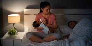 mother exhausted bottle feeding newborn while father sleeps