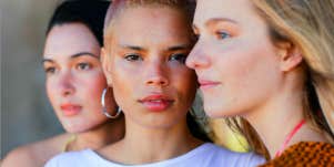 three young ladies, a pale brunette, a tawny blonde, and a pale blonde look into the camera or away wistfully, zoomed in closely.