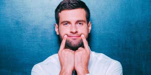 man in front of blue background trying to make himself smile with his fingers