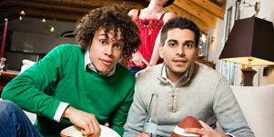 Two men watch football with woman in the background