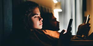 couple laying in bed looking at phones