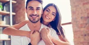 man smiling while girlfriend hugs him from behind