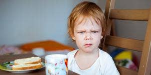angry child with sandwich and cup on the table