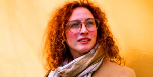 woman with red hair and glasses standing against wall