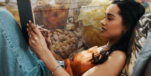 Woman watching Tv on her iPad alone, while binging snacks after work 