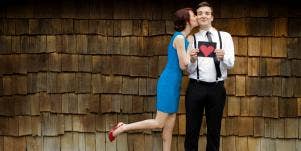 man holding a drawing of a heart while woman kisses his cheek