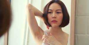 woman looking in the mirror wondering why she has armpit hair