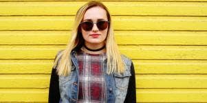 cool woman in sunglasses jean jacket smiling yellow background