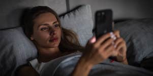 girl in bed looking at phone at night