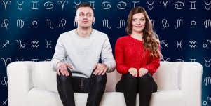 awkward couple sitting on couch in front of zodiac signs