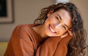 People With This Kind Of Phone More Humble & Kind, According To Research Happy young woman sitting on sofa at home and looking at camera.