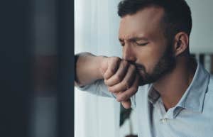 lonely sad handsome man standing near window at home