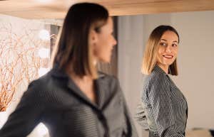 Self-confident Woman looking at her reflection into the mirror indoors