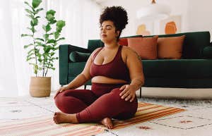 Plus size woman sitting cross legged and closed eyes in living room.