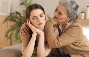 The Advice One Woman Gave Me About Divorce Should Be A Warning To Everyone Middle aged mother in law is embracing her daughter in law, comforting upset frustrated daughter in law with closed eyes, touching cheeks, sitting on couch at home.