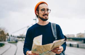 smiling male traveler walking with map having city tour excited with urban setting on autumn weekends