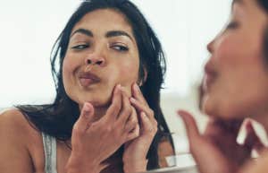woman popping pimple in mirror