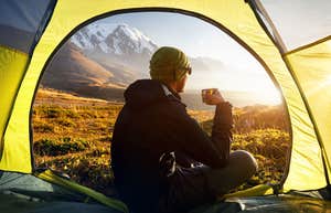 man sitting in the opening of a tent watching the sunrise