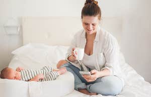 mom sitting on bed on phone while baby sleeps