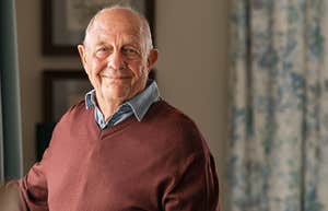 Portrait of happy retired senior man standing at home near window