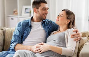 husband hugging pregnant wife and rubbing belly while sitting on couch