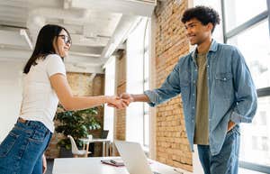 two co-workers shaking hands across a desk