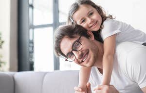 dad with young daughter on his back in front of couch