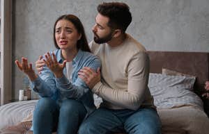 husband trying to calm down crying wife while sitting on bed